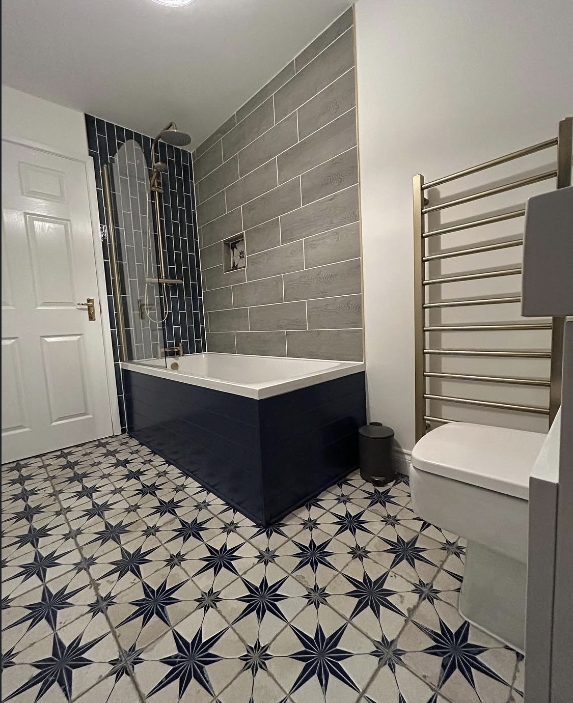 Completed bathroom with tiled shower over bath, heated towel rail and patterned floor tiles