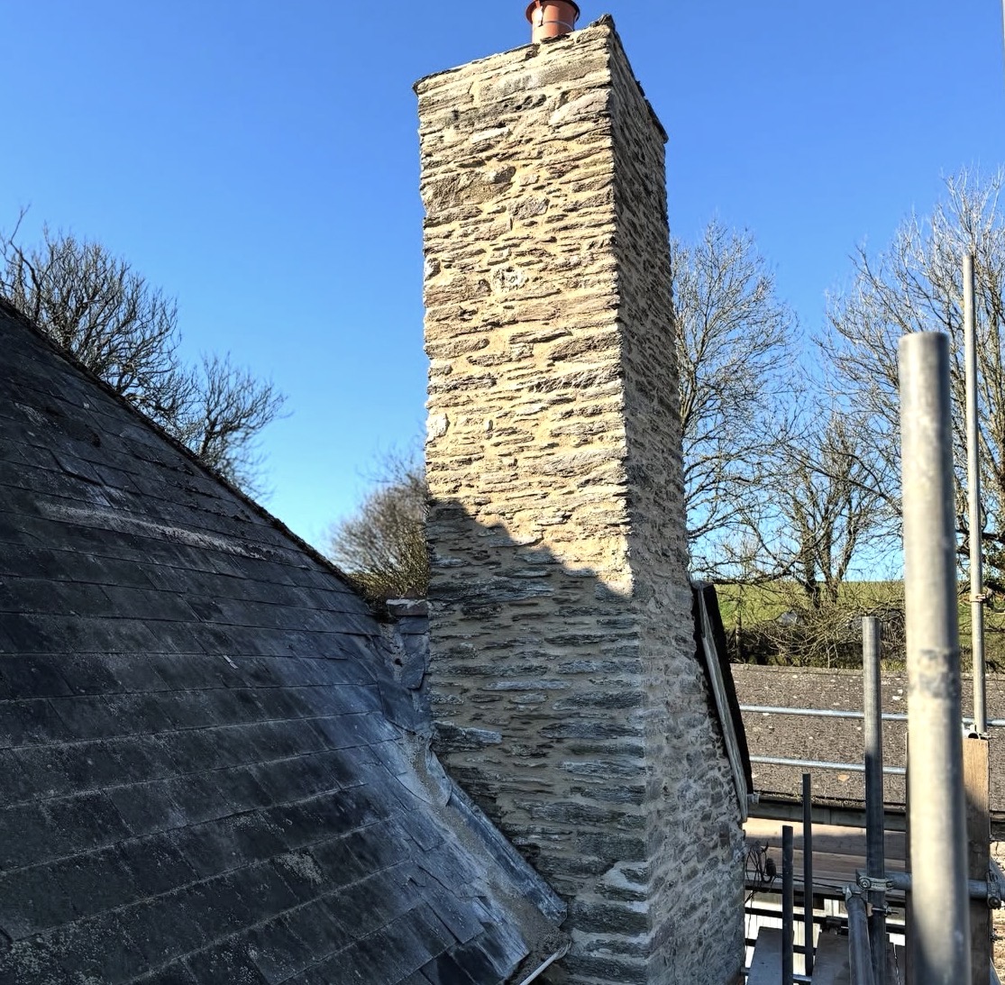 Stone chimney stack seen against a clear sky above a slate roof