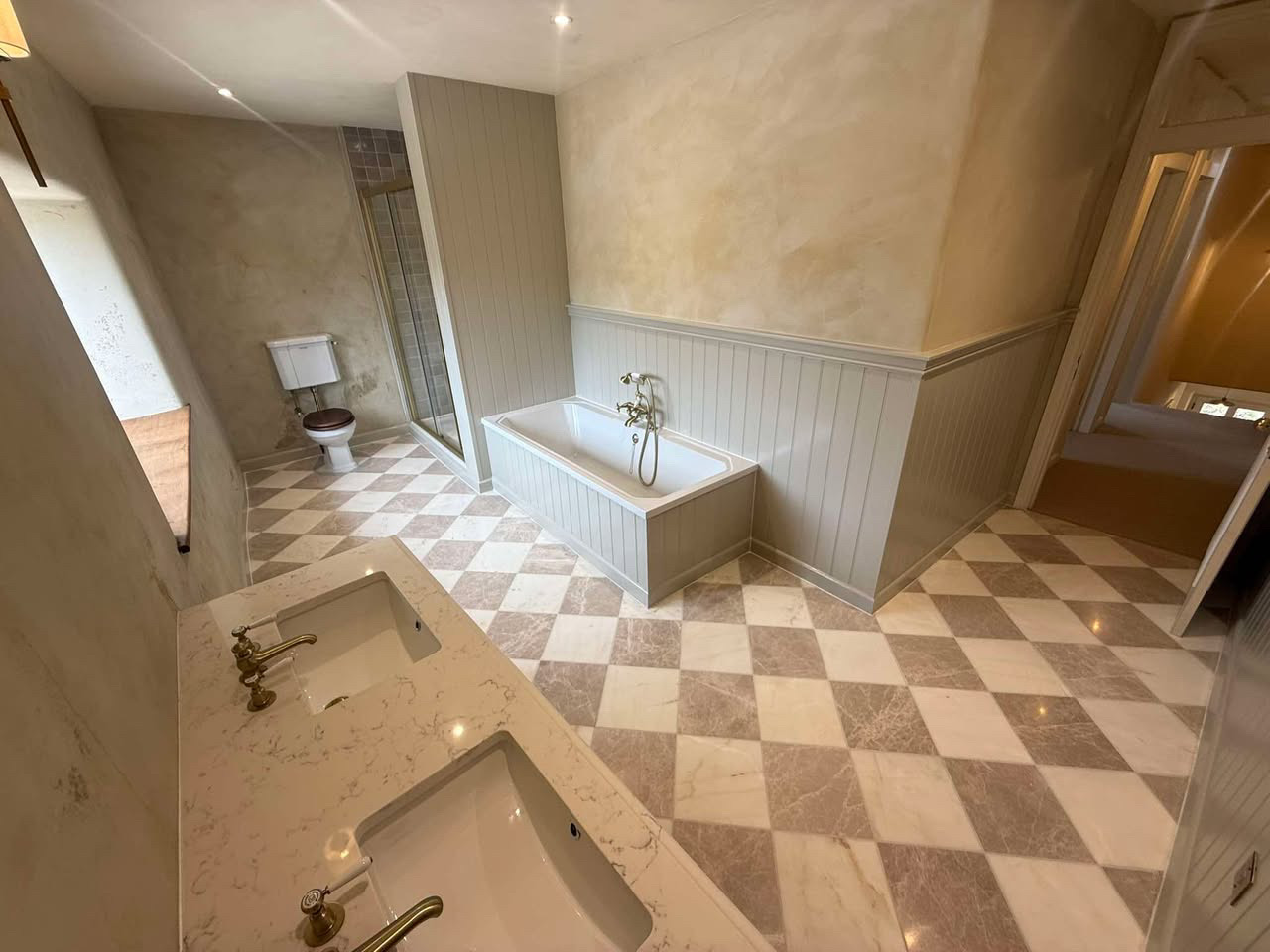 Finished bathroom with panelled bath, twin basin and chequerboard marble stone floor